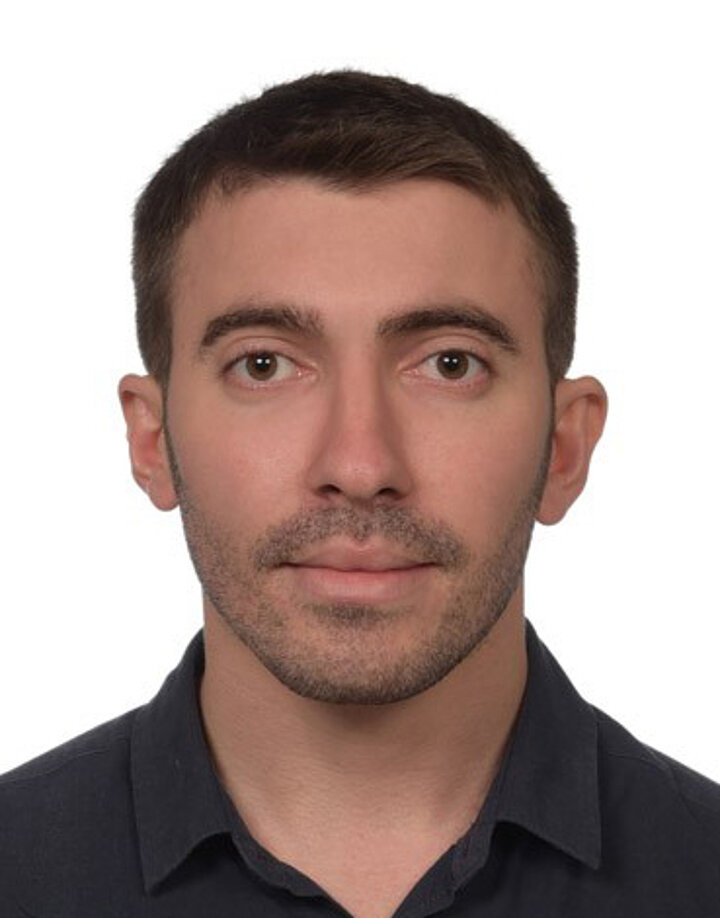 A young man with Middle Eastern facial features, wearing a dark polo shirt.