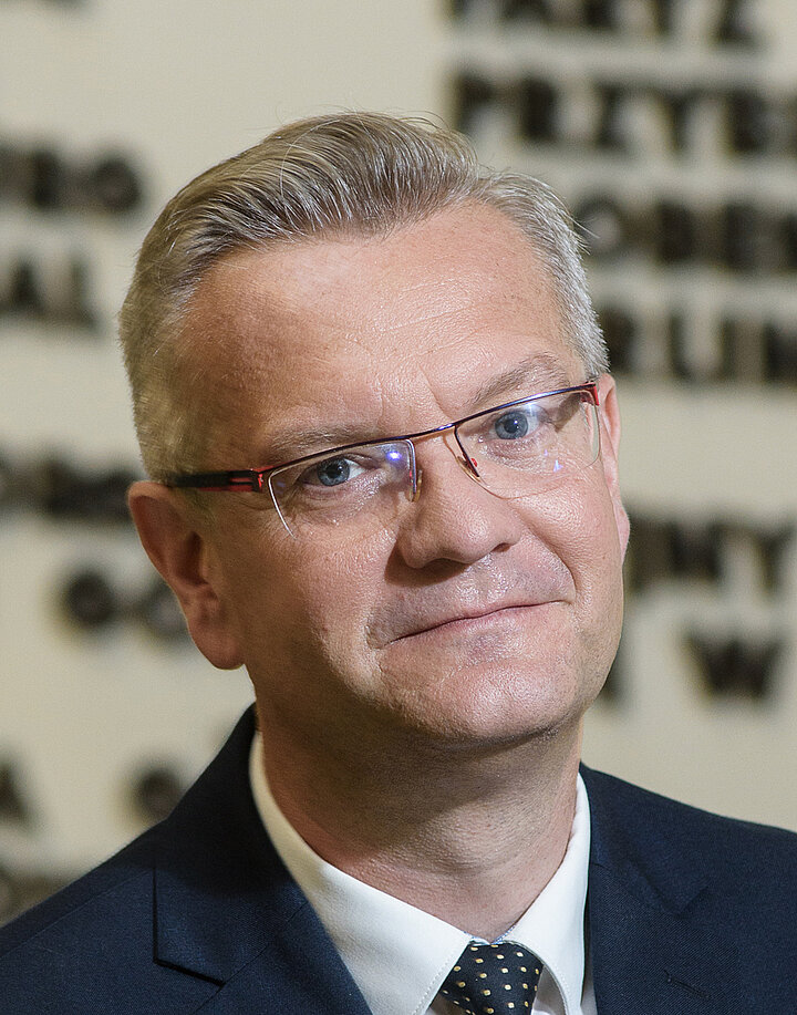 Mążczyzna w średni wieku w okularach i granatowym garniturze.