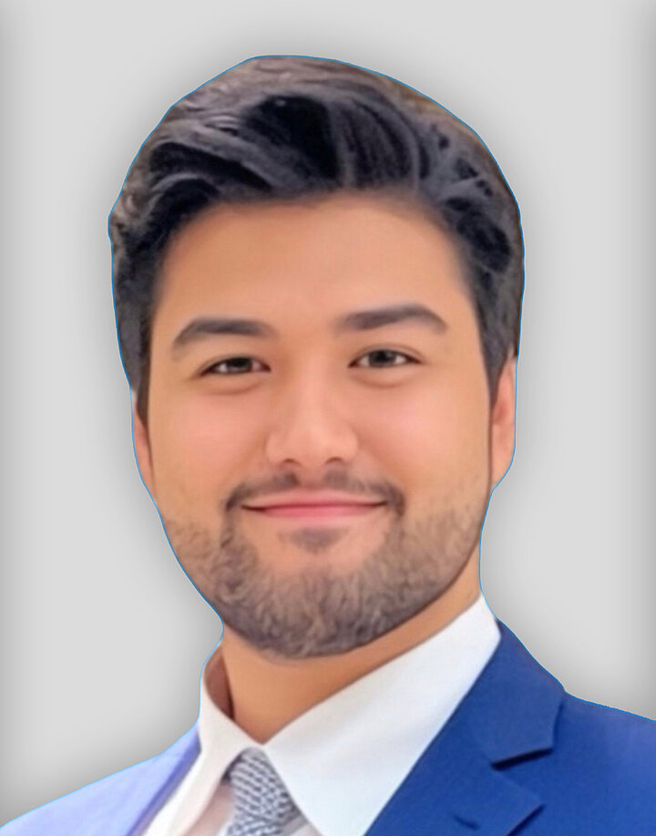 Uśmiechnięty mężczyzna o bliskowchodnich rysach i ciemnych starannie ułożonyh włosach. Nosi niebieską marynarkę.