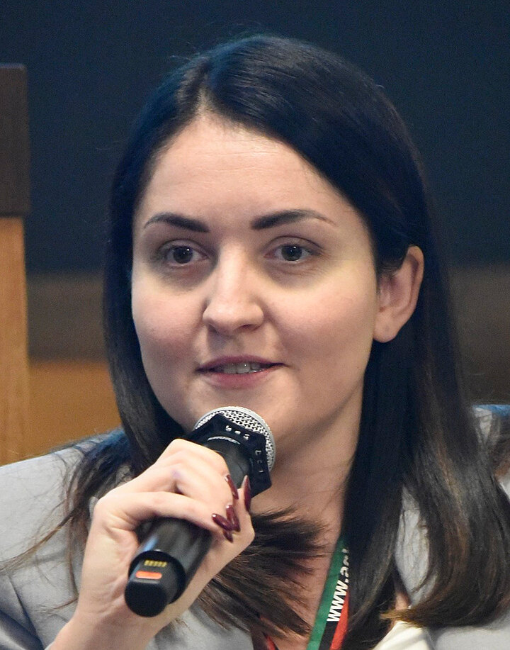 Młoda ciemnowłosa kobieta mówiąca do mikrofonu. 