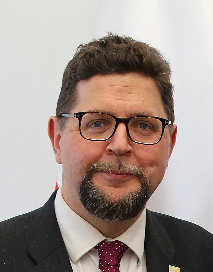 Mężczyzna z brodą w średnim wieku noszący klasyczne okulary.