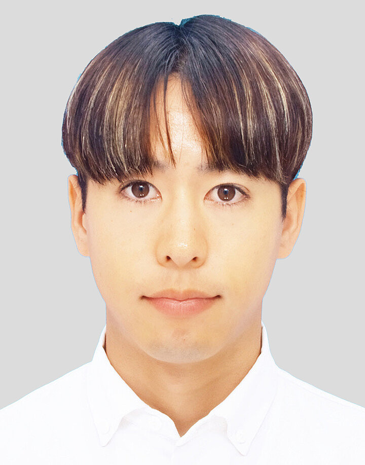 Młody mężczyzna o dalekowschodnich rysach, ciemnych prostych włosach z długą grzywką. Nosi białą koszulę.