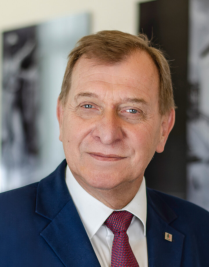 Uśmiechnięty, starszy mężczyzna w granatowtm garniturze.