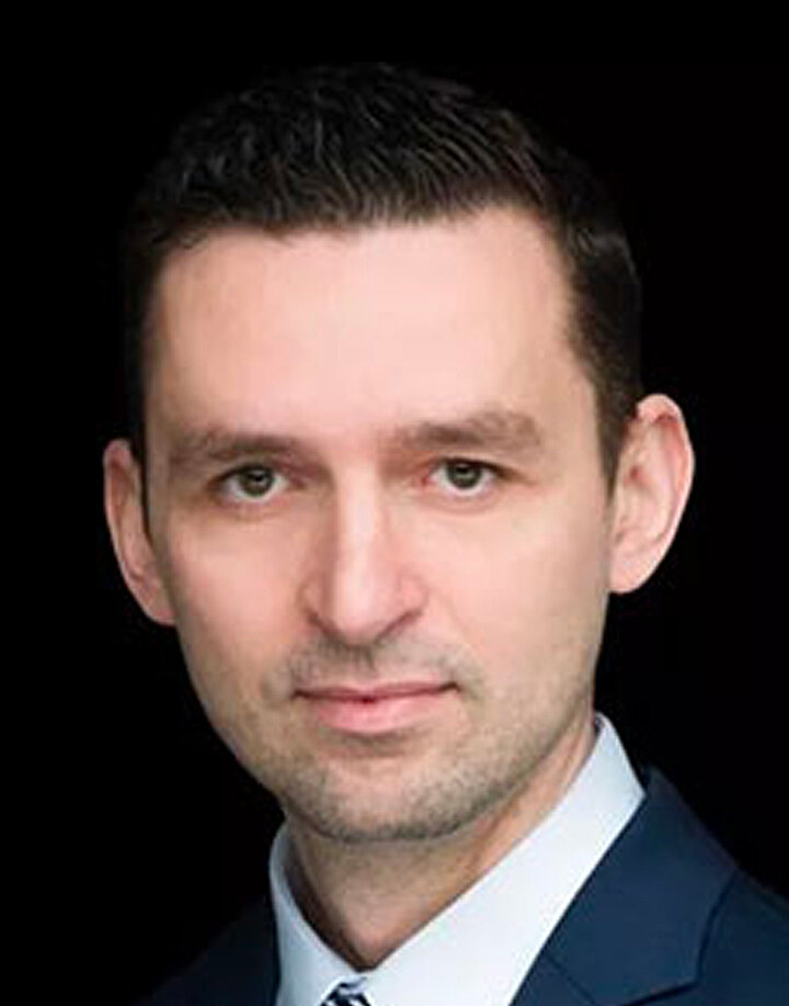 Mężczyzna w średnim wieku o kiemnych włosach, noszący granatowy garnitur.