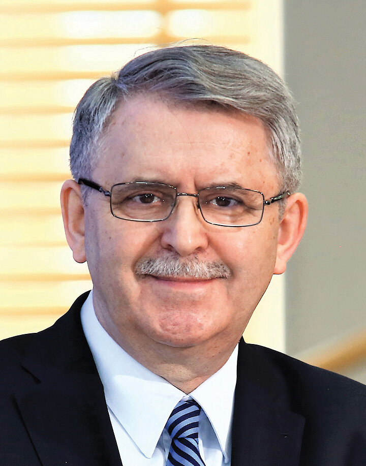 Starszy szpakowaty mężczyzna noszący wąsy oraz okulary.