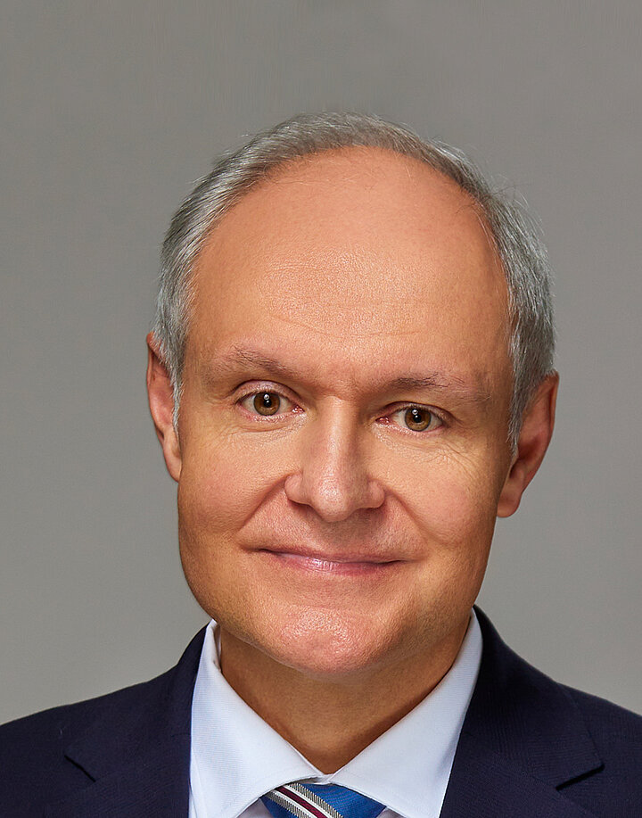 Uśmiechnięty, staerszy mężczyzna w ciemnej marynarce.