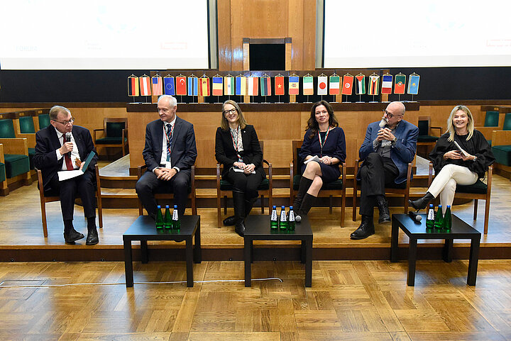 Sześcioro prelegentów siedzi w dużej zabytkowej sali.