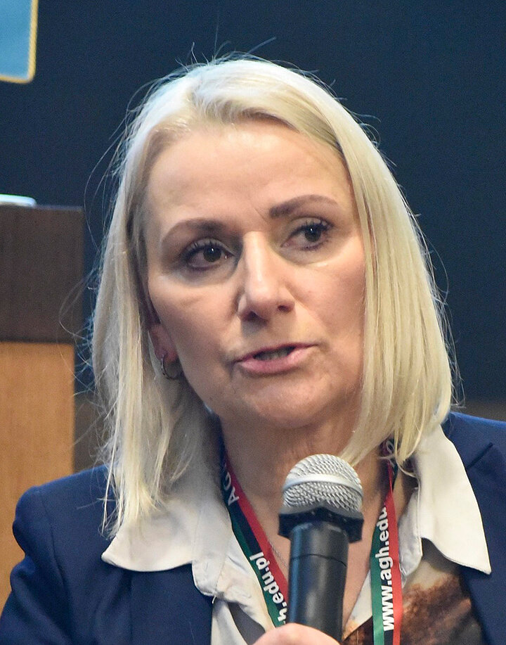 Blond włosa kobieta w średnim wieku mówi do mikrofonu.